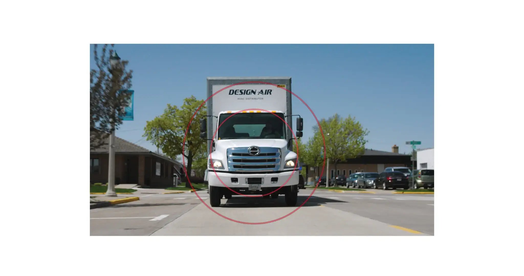 A white Hino Design Air truck, seen front-on, driving down a road on a sunny day and picked out with two red concentric circles