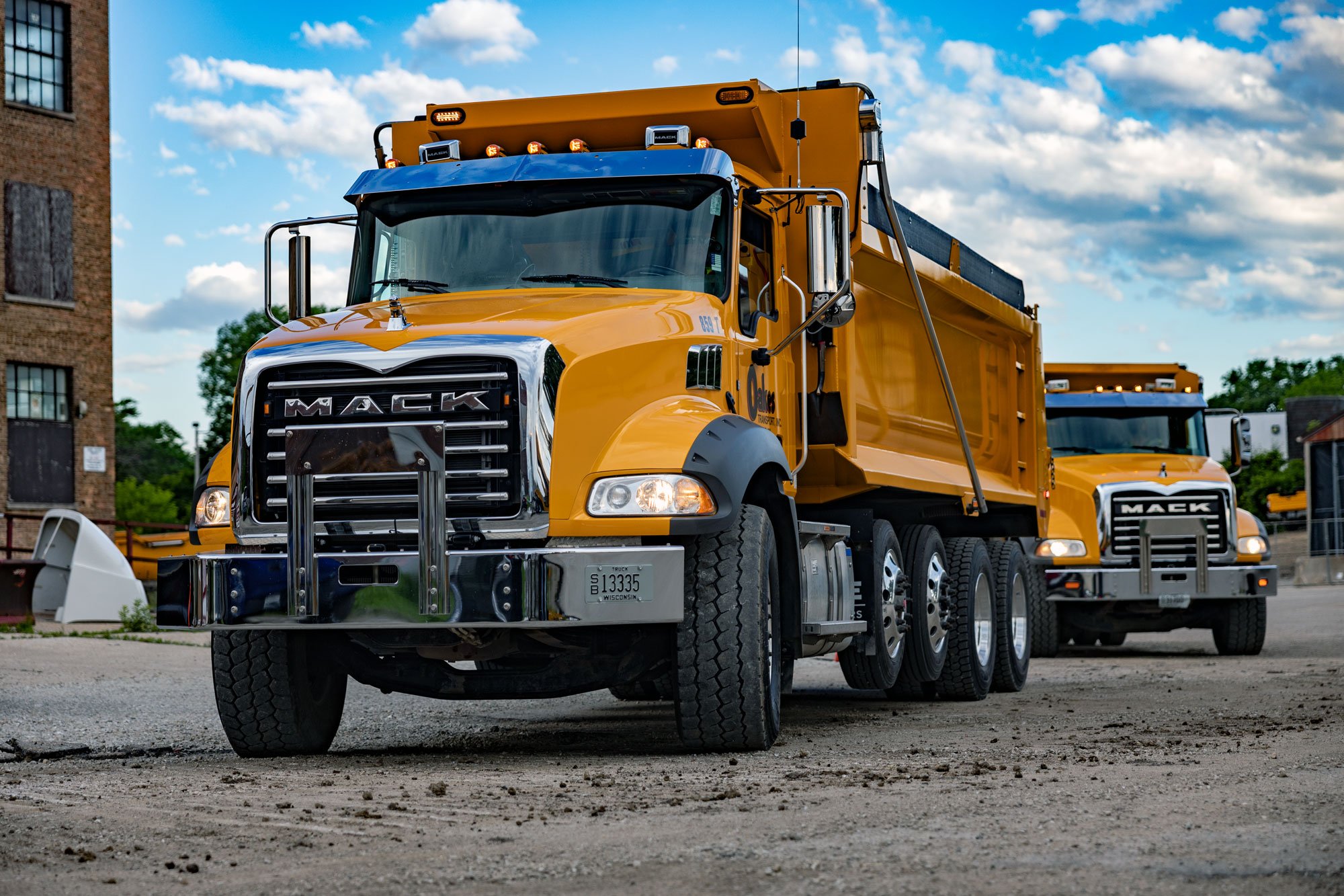Two pristine burnt orange Mack trucks approaching a site
