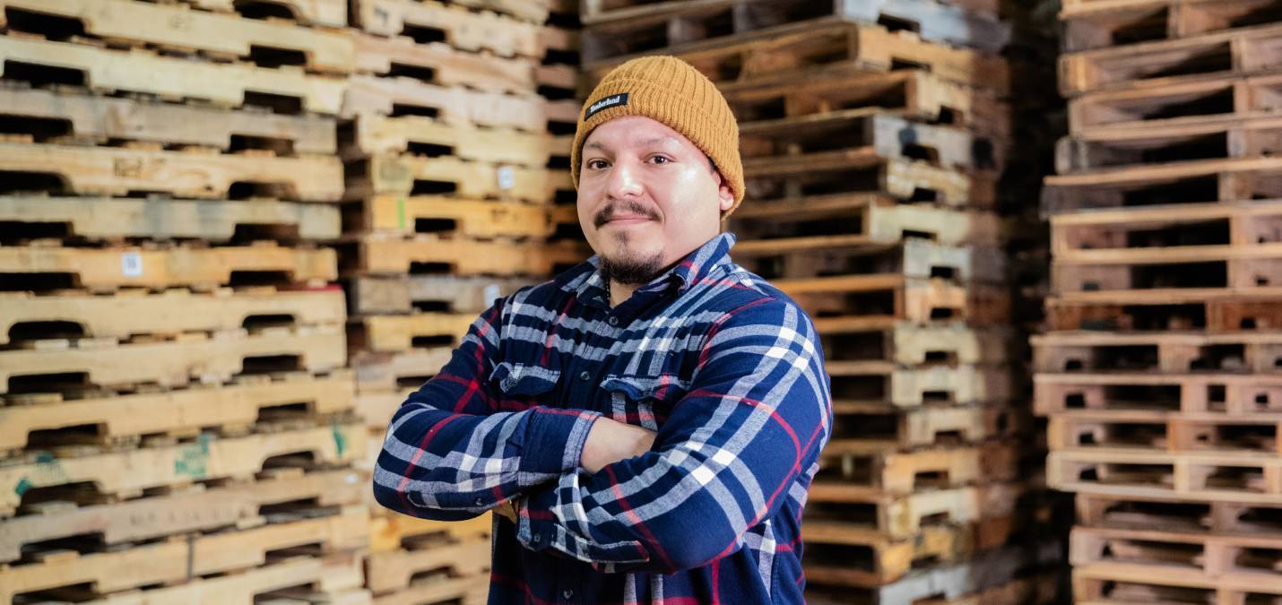 Logical & Packaging Logistics employee Daniel Villafuerte standing in front of stacked wooden pallets