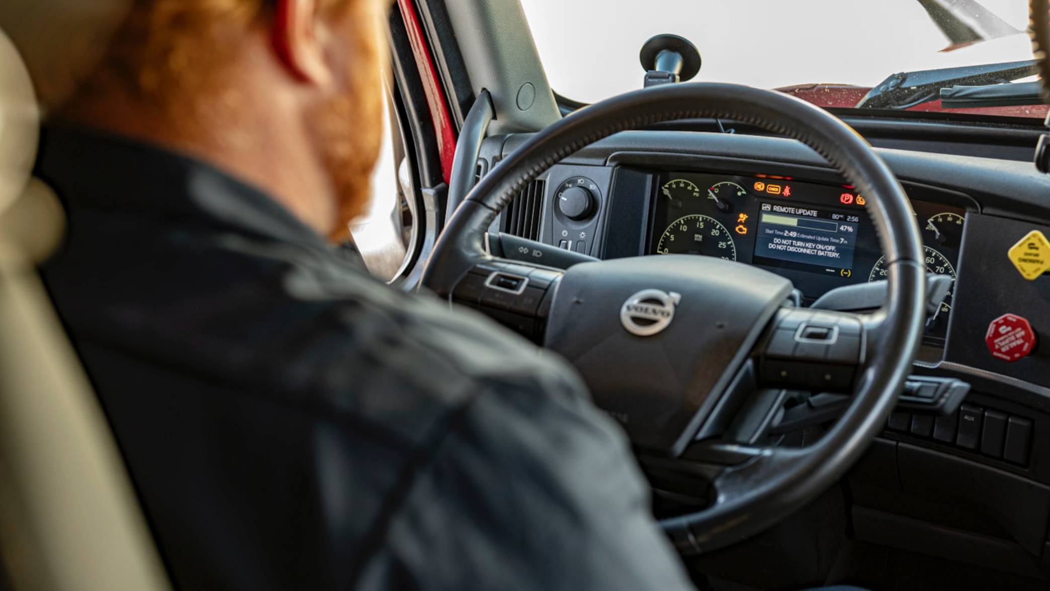 Nelson Freight Service technician in a black shirt performing remote diagnostics on a Volvo truck while sitting in the driver's seat