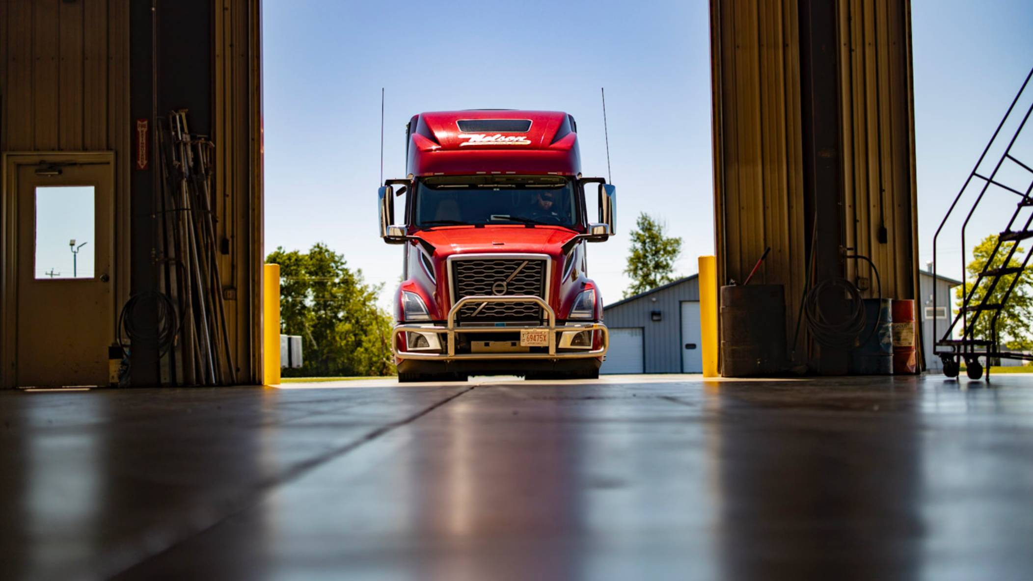 A red Volvo truck with Nelson Freight Service branding entering a warehouse