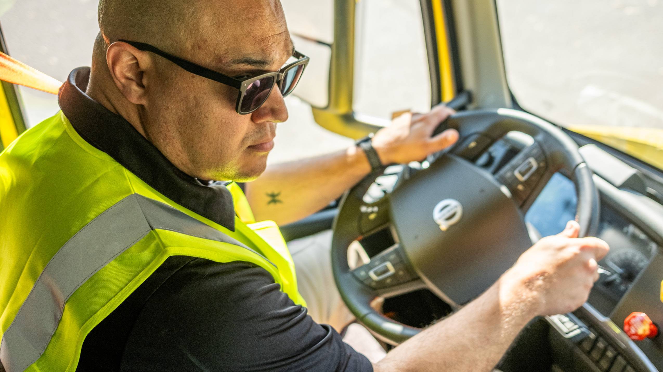 A Veriha driver in a black shirt and high-vis jacket behind the wheel of a Volvo truck
