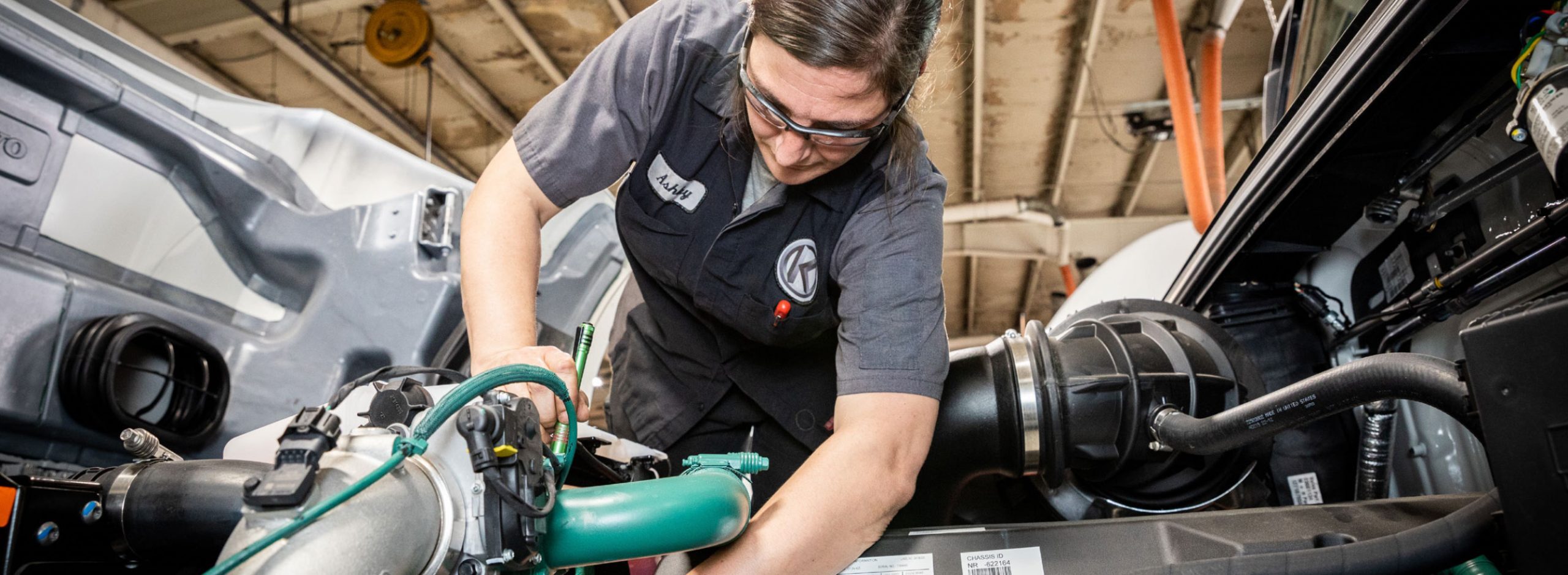 Kriete technician, Ashley, in dark gray and black overalls working on a truck engine
