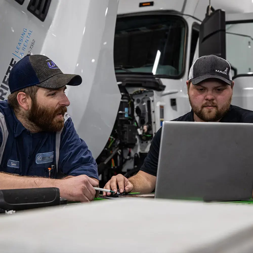Two Kriete technicians in dark uniforms and caps reviewing data on a laptop