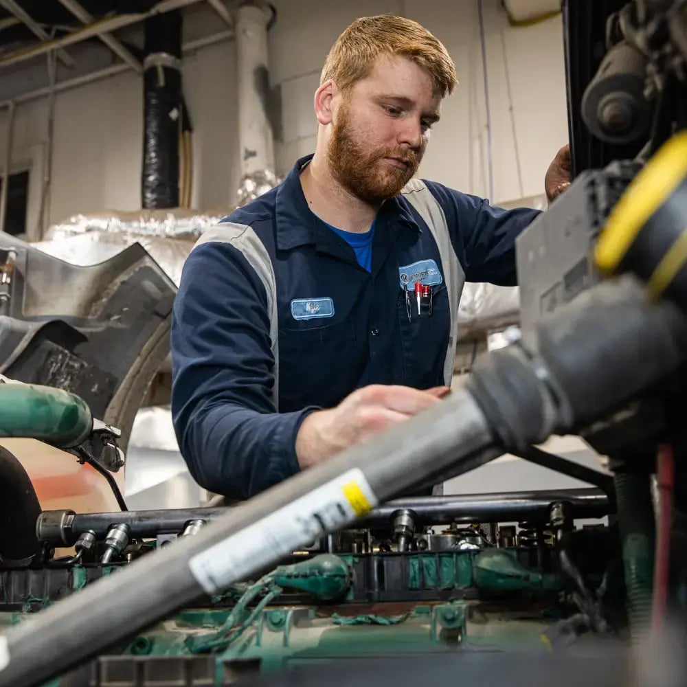 Kriete technician in a dark blue uniform with gray straps, working on a truck engine