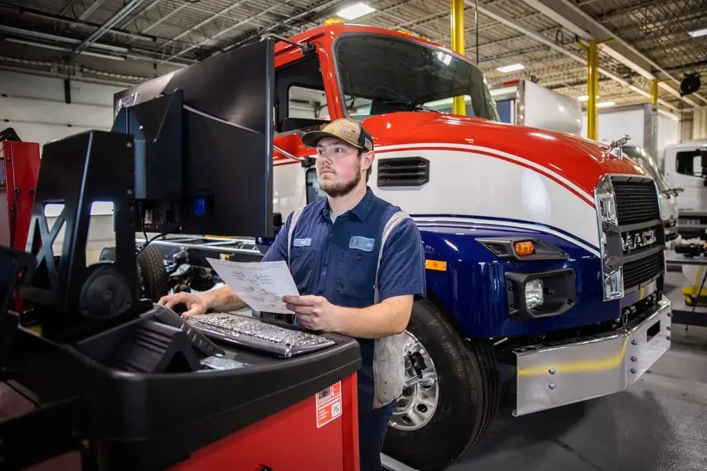 Service technician at computer assessing a red, white, and blue-striped truck