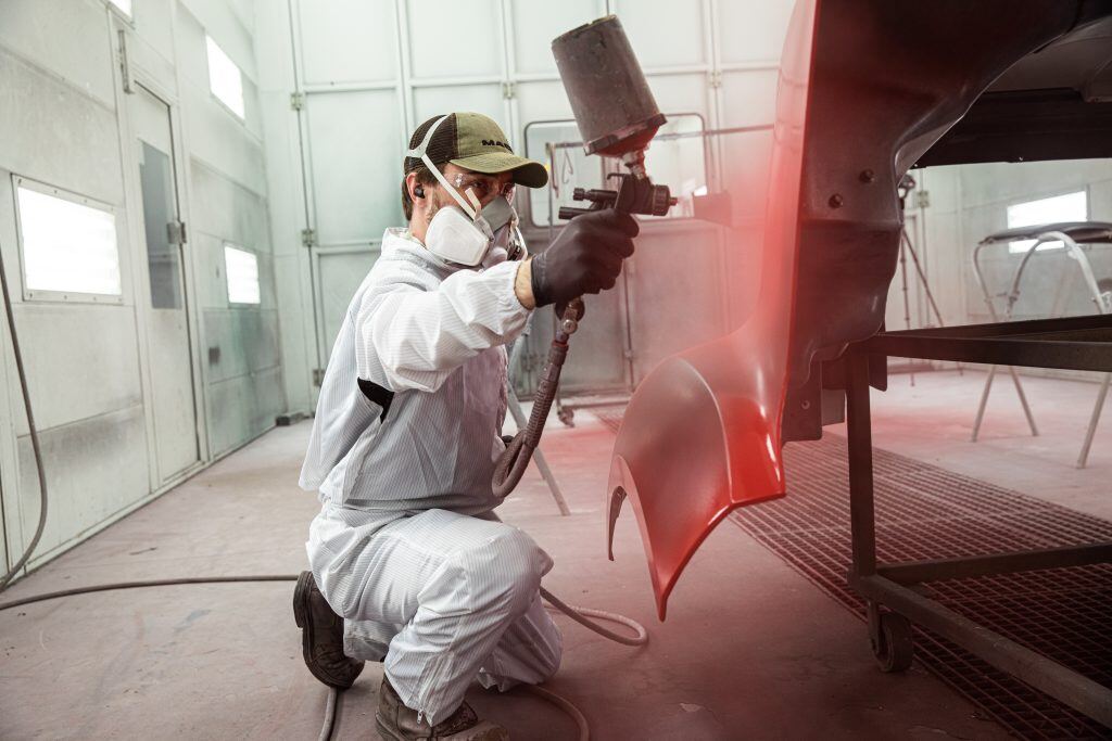 A Kriete technician in white safety clothes and mask painting a truck panel red