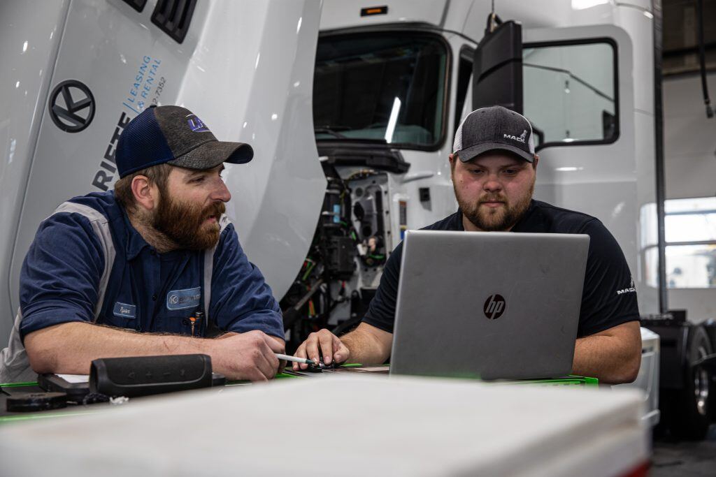 Two Kriete technicians reviewing diagnostic data on a laptop in front of a white truck