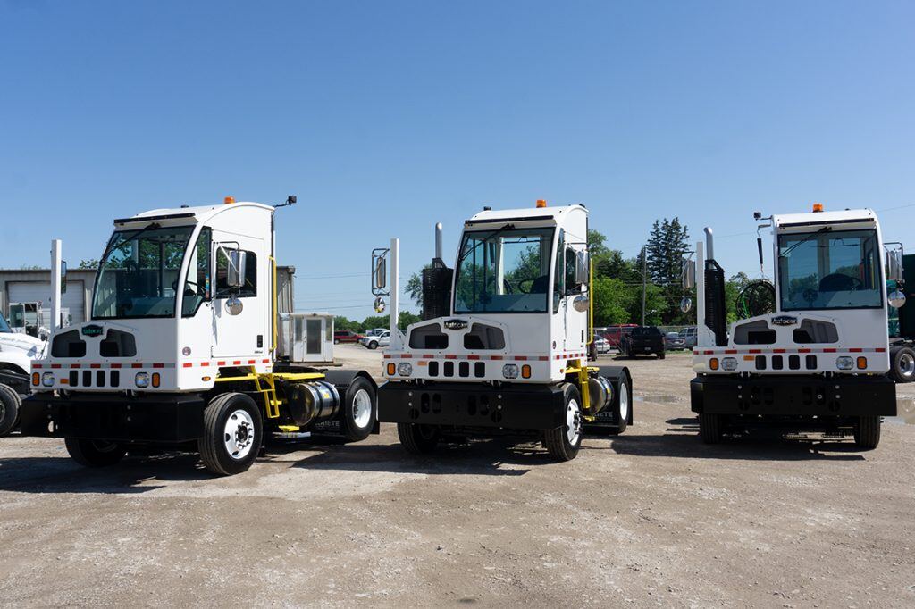 A trio of white Autocar terminal tractors beneath a clear blue sky
