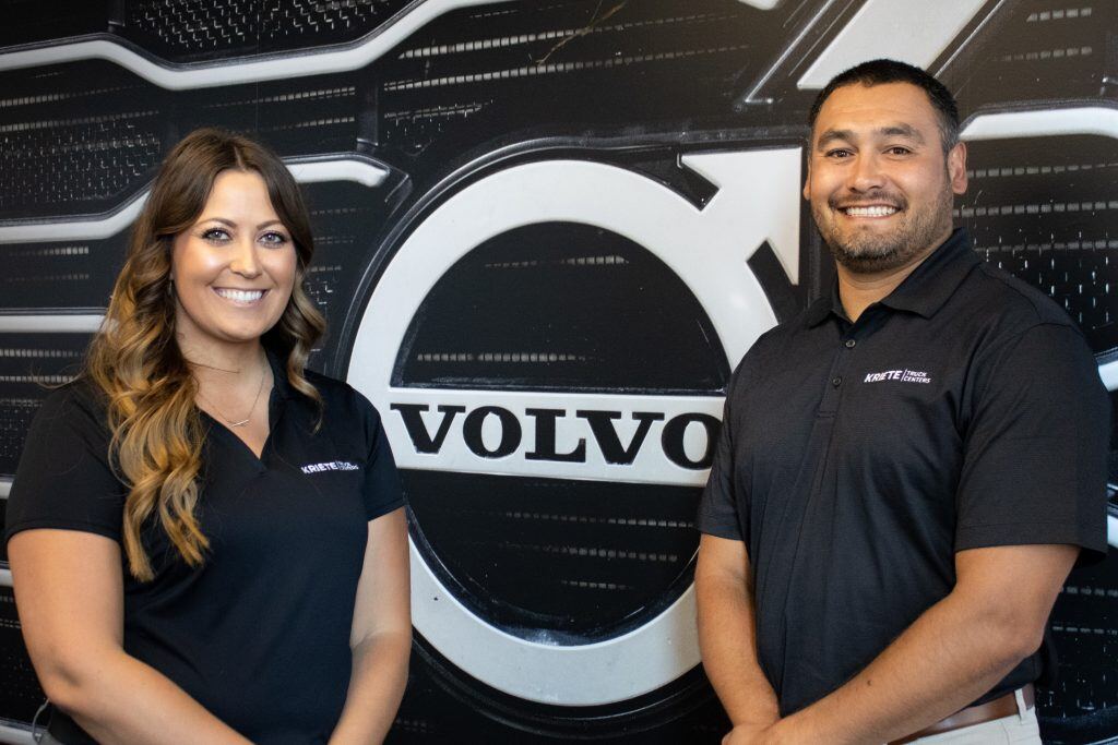 Two members of the Kriete finance and insurance team smiling in front of a large Volvo logo