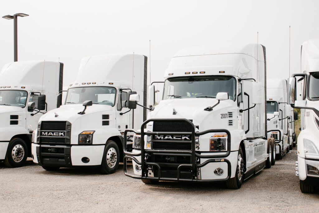 A fleet of four white Mack trucks in a row