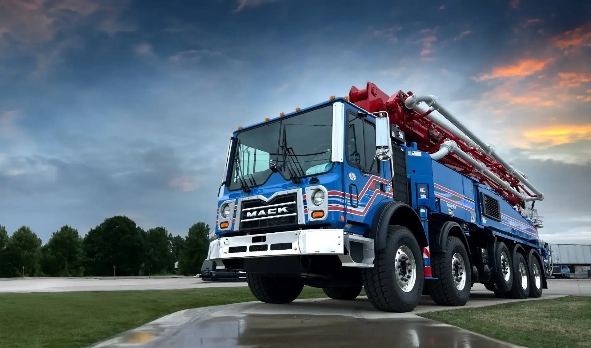 A blue and red Mack truck parked on a wet road beneath an overcast sky at sunset