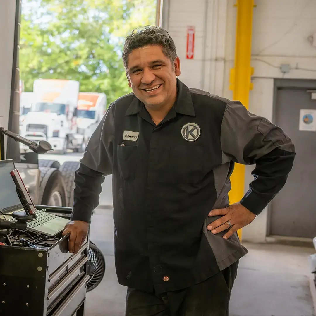 A Kriete employee in a dark gray and black shirt smiling at the camera next to a computer and other tools