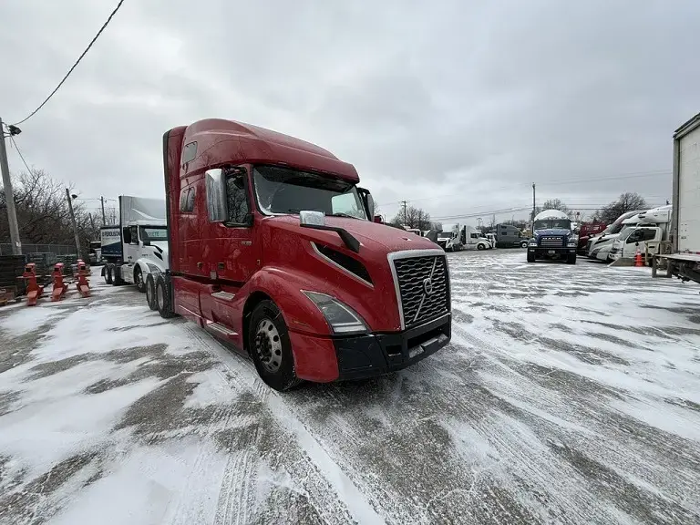 Burgundy Volvo VNL in a car park covered in a thin layer of snow beneath a cloudy sky