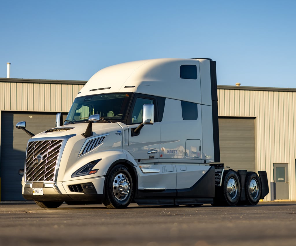 White Volvo VNL parked outside a warehouse beneath a cloudless sky